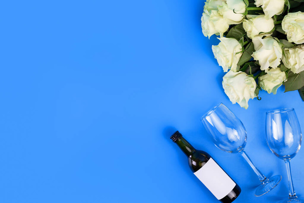Top view photo of romantic evening, dinner decor hearts love wineglasses with confetti wine bottle and white tape with large bouquet of white roses on isolated blue background with copyspace - Valokuva, kuva