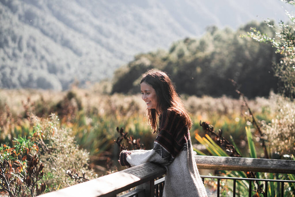 fehér barna lány barna és szürke gyapjú pulóver nyugodt és nyugodt látszó zöld táj hegyek és fák fa erkélyről, tó gunn, új-Zéland - utazási koncepció - Fotó, kép