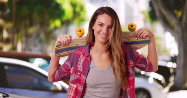 Πορτρέτο του χαμογελαστού κοριτσιού χιλιετηρίδας ποζάρουν με skateboard στους ώμους στο κέντρο. Πορτρέτο του γέλιου γυναίκα σκέιτερ κρατώντας skateboard έξω στο δρόμο της πόλης. 4ια - Πλάνα, βίντεο