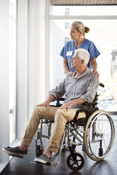 Taking him around to see the views. Full length shot of a mature female nurse and her senior male wheelchair-bound patient in the hospital - 写真・画像