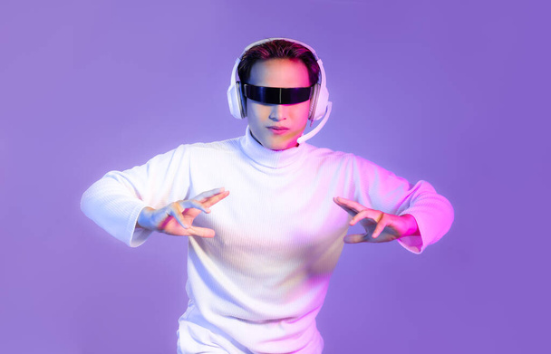 Aziatische man dragen vr bril en koptelefoon set spelen spel online paarse neon kleur achtergrond. Metaversaal concept. - Foto, afbeelding