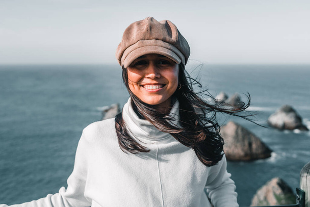 joven mujer caucásica con el pelo largo desaliñado sonriendo a la cámara feliz desde el mirador sobre el mar y las rocas en un buen día, punto de pepita, Nueva Zelanda - Concepto de viaje - Foto, imagen