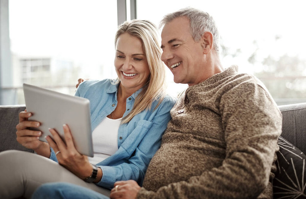 Τριγυρνάω στο διαδίκτυο. ένα ώριμο ζευγάρι που χρησιμοποιεί ένα ψηφιακό tablet ενώ χαλαρώνουν μαζί στον καναπέ στο σπίτι - Φωτογραφία, εικόνα