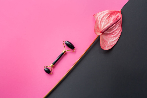Onyx massage guasha face roller and Anthurium on pink and black background. Massage tool for facial skin care, SPA beauty treatment concept. Space for text. Flatlay - Foto, imagen