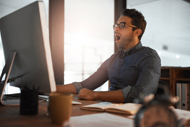 Он проявляет самоотверженность даже от истощения. молодой бизнесмен зевает во время работы за компьютером в офисе - Фото, изображение