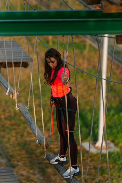 Chica aventura mirando hacia abajo mientras está de pie sobre el pilar de madera en el parque de aventuras - Foto, Imagen