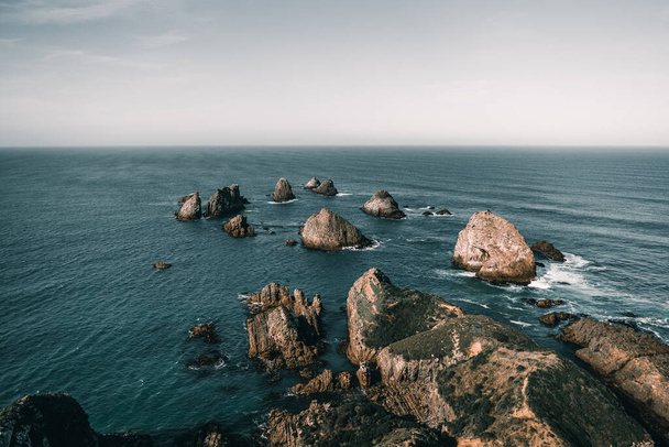 paisagem calma de pedras e rochas encontrada no meio do oceano em um dia calmo, com poucas ondas sob um céu azul com poucas nuvens, ponto nugget, Nova Zelândia conceito de viagem - Foto, Imagem