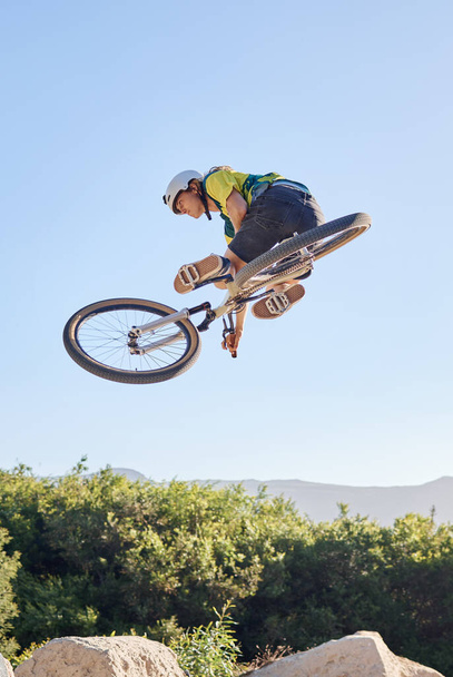 Bike, extreme sport and outdoor fitness, man does dangerous stunt, sports motivation and training in nature. Exercise, athlete with mountain bike, risk and active with energy and jump over rocks - Φωτογραφία, εικόνα