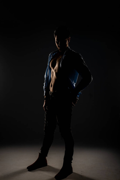 Sideview of an handsome model taking off his shirt and posing inside the studio - Foto, Imagem