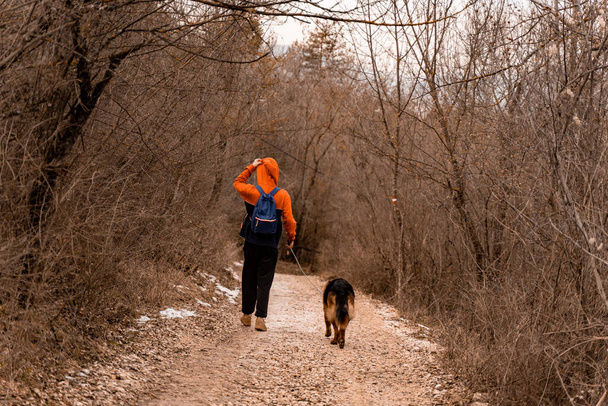 Bello e fantastico ragazzo sta portando il cane da solo sul sentiero della foresta mentre si gode il suo tempo e si mette il cappello - Foto, immagini