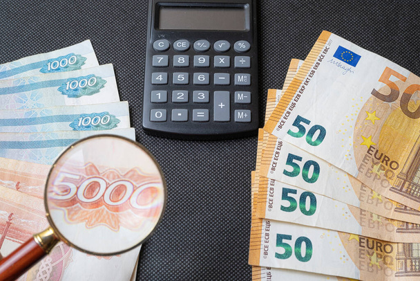 Siyah arkaplan, hesap makinesi ve büyüteç üzerinde Rus rublesi ve avrosu - Fotoğraf, Görsel