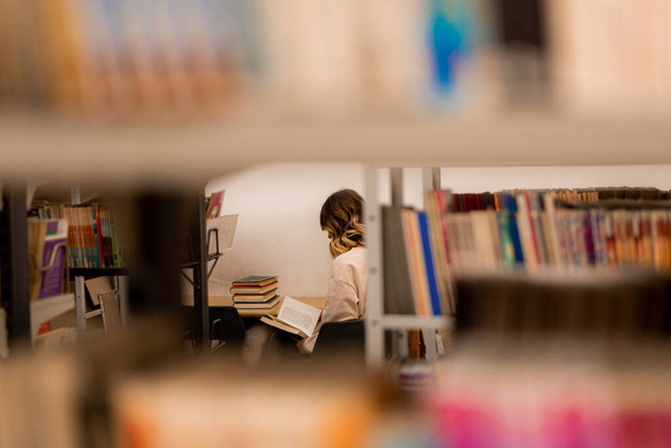 Meisje aan de andere kant van de planken studeert voor de universiteit in een bibliotheek - Foto, afbeelding