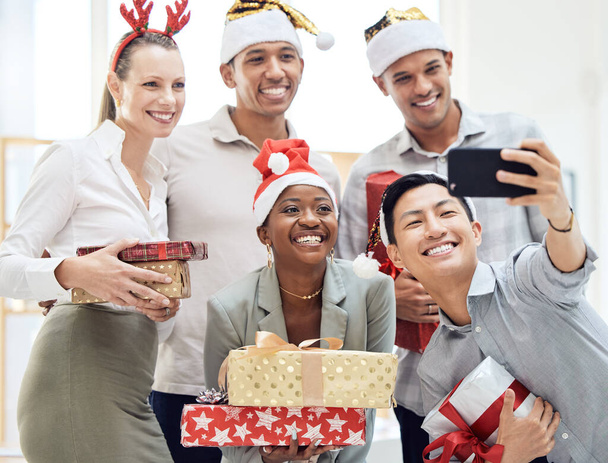 Счастливое, офисное и праздничное селфи корпоративного мероприятия с сотрудниками на телефоне. Деловой работник, друзья и сотрудники группы вместе с улыбкой, подарком и праздником. - Фото, изображение