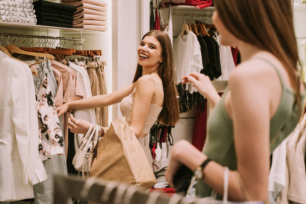 Két csinos bevásárló lány nézi a ruhákat a divatboltban. - Fotó, kép