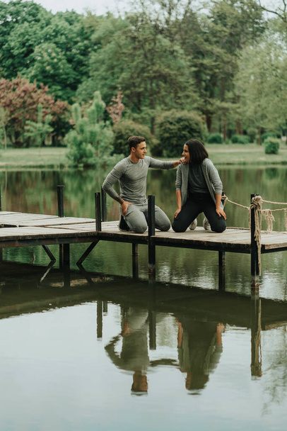 Starkes Paar macht Auszeit vom Training, während es auf der Brücke im Park am See sitzt - Foto, Bild