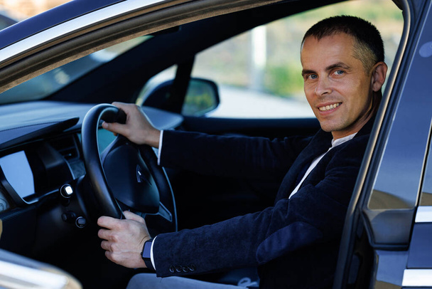 Lviv, Ukraine - October 17, 2022: Portrait of handsome businessman smiling while driving a new tesla model x electric car. Young handsome man is sitting in luxury electric car. Bearded man is driving. - Foto, Bild