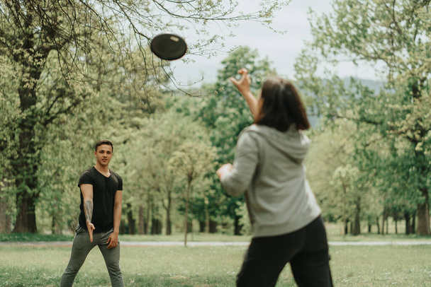 Schönes Paar spielt Frisbee, während es auf dem Rasen im Park steht - Foto, Bild