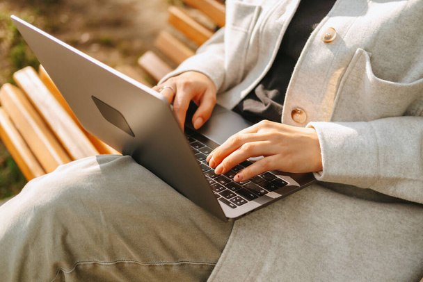 Fechar foto de mãos femininas digitando no laptop enquanto sentado em um banco no parque. - Foto, Imagem
