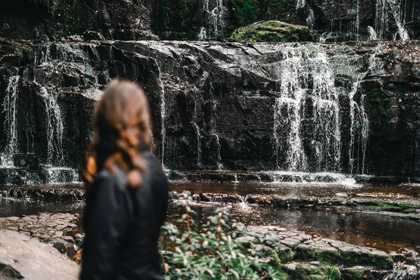 morena caucásica desenfocada desde atrás contemplando las hermosas y tranquilas cascadas junto a las rocas del lago en medio del bosque y la naturaleza, cascadas purakaunui, Nueva Zelanda - Viajar - Foto, imagen