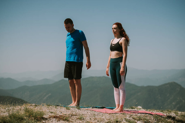 Yoga yapan çift dağın tepesinde yoga minderlerinin üzerinde duruyor. - Fotoğraf, Görsel