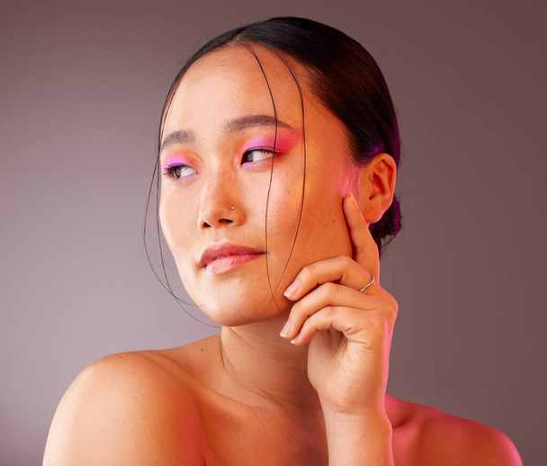 Beauty, makeup and asian woman with colourful eyeshadow isolated against a studio background. Cosmetics, glowing skin and chinese woman with glamour eye makeup. Smooth and perfect skin after a facial. - Photo, Image
