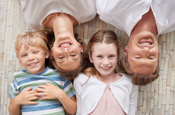 Family, children and portrait of faces with a girl, boy and parents lying on ground or floor of home together from above. Love, happy and smile with a mother, father and kids bonding in the house. - Foto, imagen