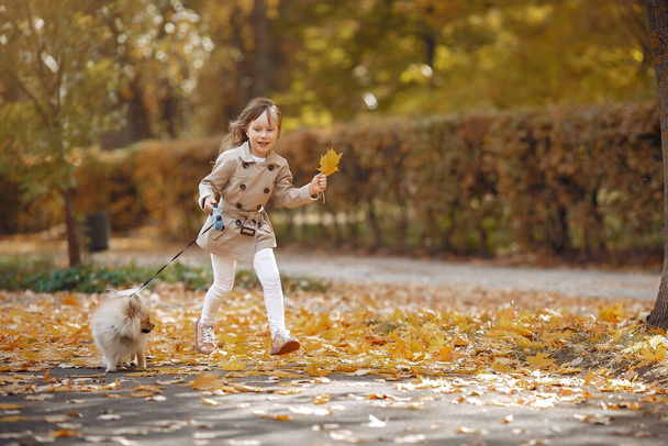 Słodkie dziecko w jesiennym parku. Elegancka mała dama z psem. Dziewczyna w brązowym płaszczu. - Zdjęcie, obraz