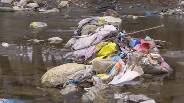 FERMER : Pile de déchets pris entre les rochers au milieu de la rivière. Des débris de rivière et des déchets plastiques se mélangent sur les pierres de la rivière. Besoin urgent de gestion des déchets et d'éducation écologique. - Séquence, vidéo