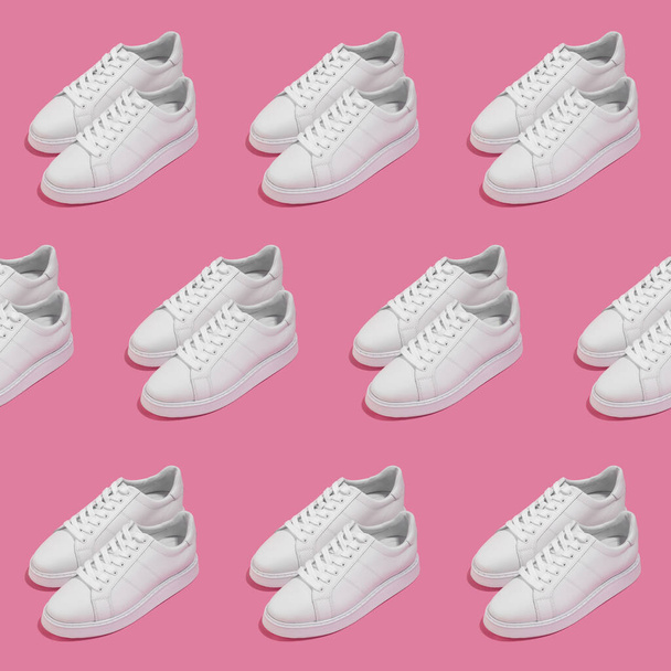Herhalend patroon van een paar witte vrouwelijke sneakers op roze achtergrond - Foto, afbeelding