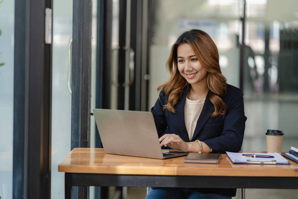 Азиатская женщина-бухгалтер сидит за рабочим столом с ноутбуком и рассчитывает финансовый график, показывающий результаты успешного инвестиционного планирования. - Фото, изображение