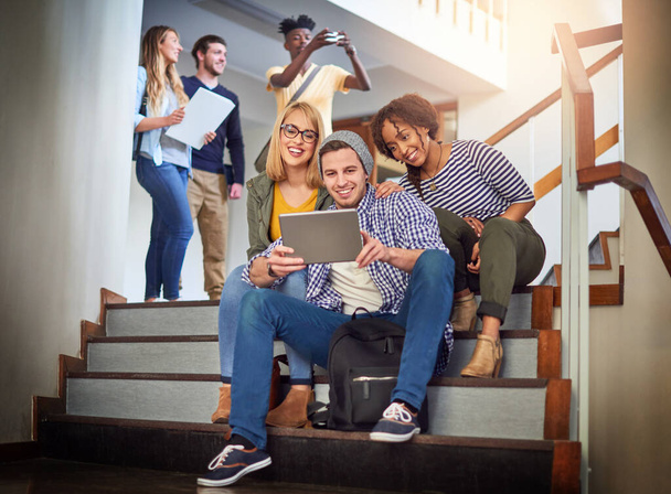 Ponerse al día con algunas conexiones rápidas. un grupo de estudiantes universitarios que utilizan una tableta digital en la escalera del campus - Foto, imagen