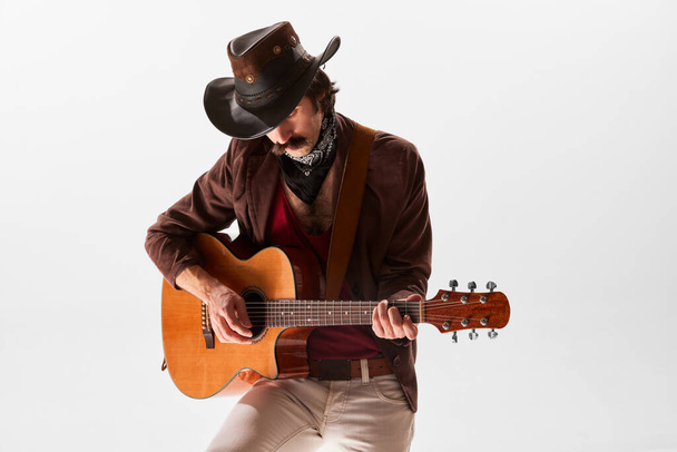 Portrait of man with moustaches in country style clothes playing guitar isolated over white background. Romantic music. Concept of music, creativity, inspiration, hobby, lifestyle, emotions - Foto, Imagen