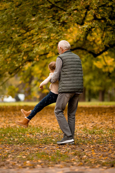 Handsome grandfather spending time with his granddaughter in park on autumn day - Photo, Image