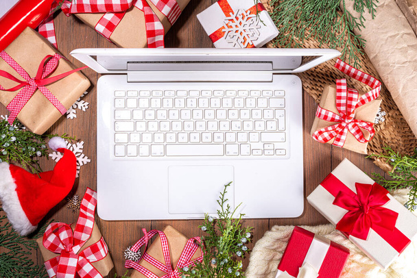 Laptop mit Weihnachtsgeschenkboxen von oben auf hölzernem Hintergrund. Notizbuch mit Geschenken, Tanne und Winterdekor. Vorbereitung auf Weihnachten, Neujahr - Foto, Bild