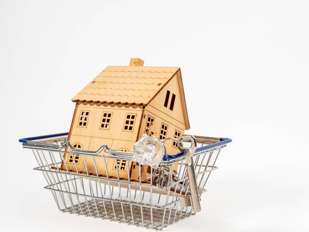 Casa de madeira em um carrinho de compras em um fundo branco. O conceito de comprar uma casa. - Foto, Imagem