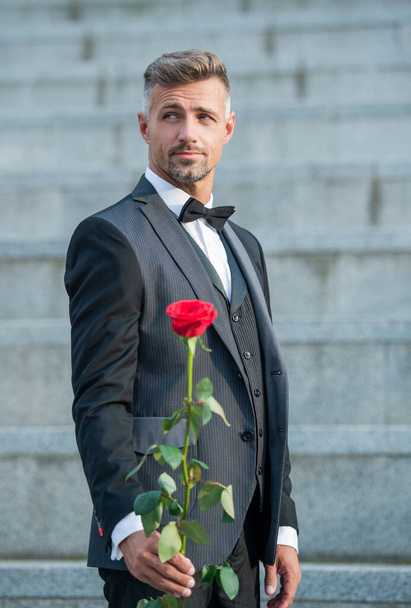 love rendezvous concept. charismatic tuxedo man with love rose. flower gift for love day. - Foto, imagen
