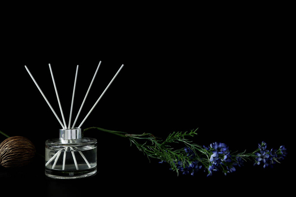 luxe geur riet diffuser glazen fles is op zwart houten tafel met bloemen te creat romantisch en ontspannen ambient in donkere slaapkamer met zwarte cement muur achtergrond op gelukkige Valentijnsdag - Foto, afbeelding