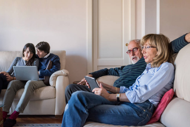 Starsza para siedzi na kanapie w domu za pomocą tabletu - Zdjęcie, obraz