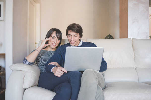 Усміхнена молода пара сидить на дивані вдома, використовуючи комп'ютерні покупки онлайн або дивитися потокове відео
 - Фото, зображення
