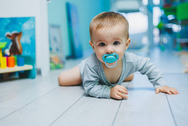 baba pelenka szelektív fókusz kisgyermek a háttérben ül a gyermek bili otthon a padlón teljes hosszában mellbimbó cumi a szájban elölnézet másolási hely - Fotó, kép