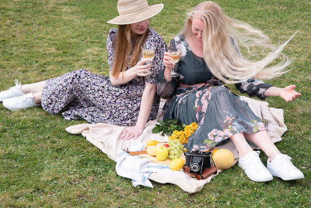 μια δύο νεαρές γυναίκες σε ένα καλοκαιρινό μακρύ φορέματα στηρίζεται σε ένα πικνίκ, μια κουβέρτα με τυρί πιάτο και φρούτα, υπόλοιπο από ανησυχίες και οικιακές δουλειές, πάρκα και χώρους αναψυχής, .High ποιότητας φωτογραφία - Φωτογραφία, εικόνα