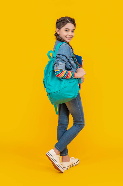 Happy teenager carrying backpack, education. Teenage girl yellow background. School education. Informal and non-formal education. - Foto, afbeelding