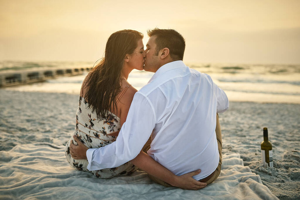 Keeping the romance alive. High angle shot of an affectionate young couple kissing while sitting on the beach - Photo, Image