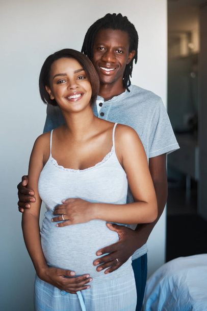 Улыбки на наших лицах говорят сами за себя. Портрет счастливого молодого человека, позирующего с беременной женой дома - Фото, изображение
