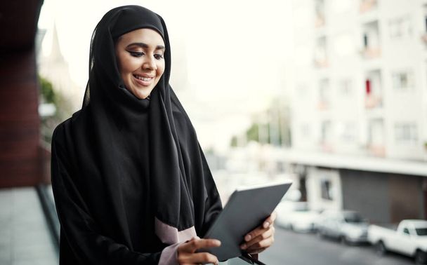İşler iyi gidiyor. İş yerinin balkonunda beklerken tablet kullanan geleneksel İslami giysiler giymiş çekici genç bir iş kadını. - Fotoğraf, Görsel