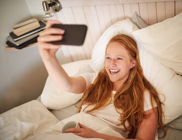 Selfie matutino, me desperté así. una joven mujer tomando una selfie acostada en la cama en el dormitorio en casa - Foto, Imagen