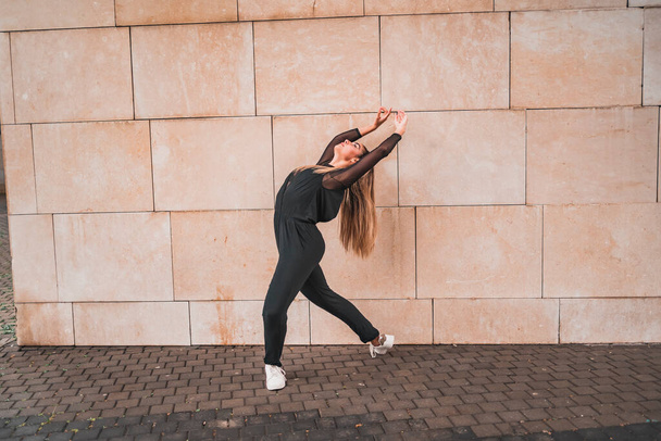 Full body side view of slim young female in black leggings and white sneakers standing on paved street and stretching body - Foto, Imagem
