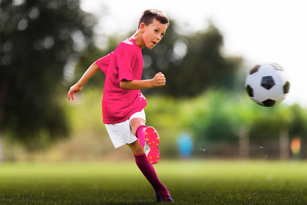 Мальчик пинает футбольный мяч на спортивном поле
 - Фото, изображение