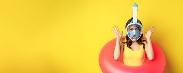 Funny happy woman in swimming ring, wearing snorkling mask for diving, posing against yellow background. Copy space - Photo, Image