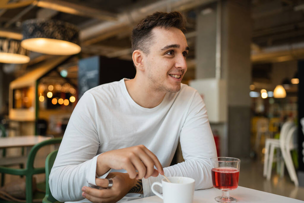 Ein Mann junge erwachsene kaukasische Mann sitzen im Café oder Restaurant allein und schauen zur Seite mit einer Tasse Kaffee echte Menschen kopieren Raum glückliches Lächeln - Foto, Bild